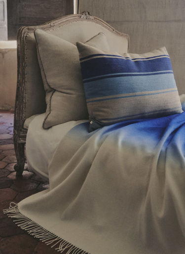 Bed with 2 pillows, beige and blue with a white and blue throw